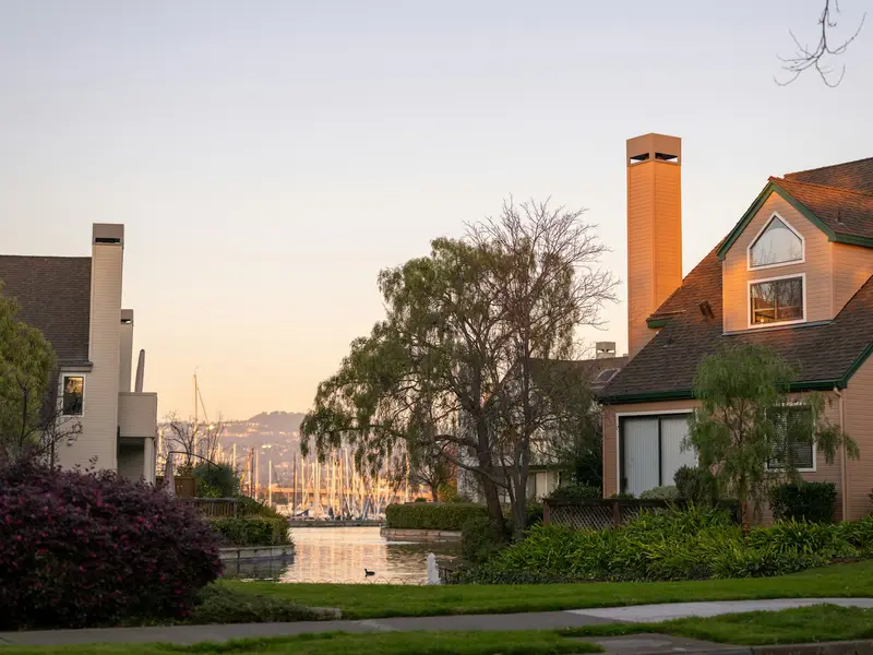 Homes along an Alameda lagoon at sunset, with sailboat masts in the distance